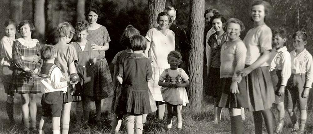 Eine Gruppe Kinder steht mit Erzieherinnen in einem Waldstück.