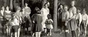 Eine Gruppe Kinder steht mit Erzieherinnen in einem Waldstück.