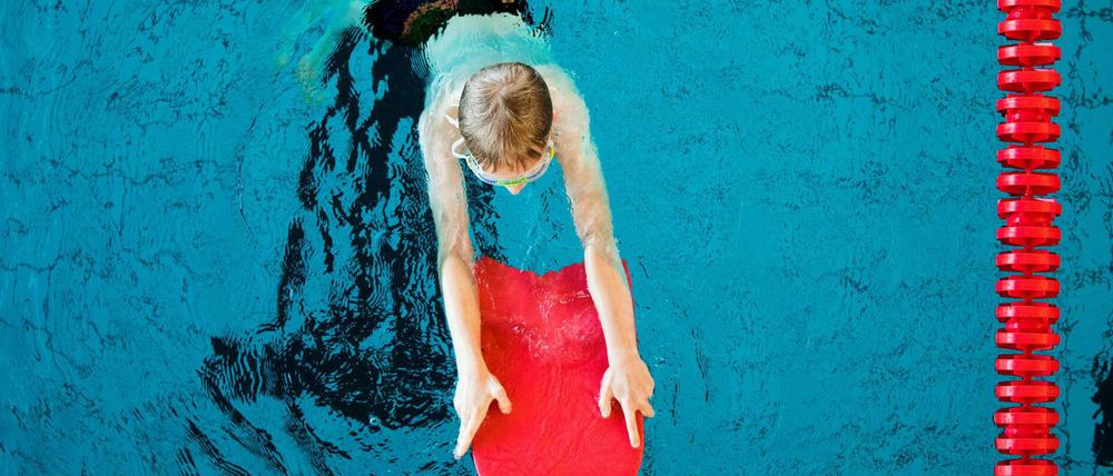 Kind mit Schwimmbrett im Wasser.