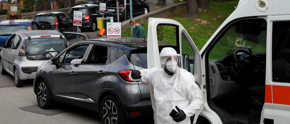 Ein Klinikmitarbeiter weist Patienten ein, die in einer langen Autoschlange warten.