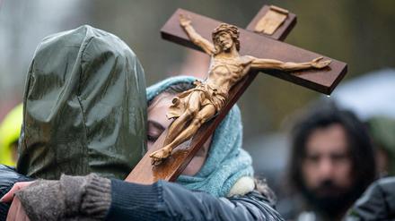 Zwei Teilnehmer der Demonstration gegen die Corona-Einschränkungen am Brandenburger Tor umarmen sich und halten ein Holzkreuz in der Hand.