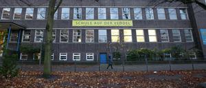 Blick auf die Ziegel-Fassade eines Schulgebäudes , auf einemm Fußweg läuft ein Kind davor entlang.