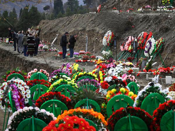Vor einer Prozession trauernder Angehöriger auf einem Friedhof sind bunte Grabgestecke zu sehen.