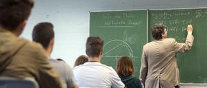 Ein Mathelehrer steht an der Tafel, die Schüler hören zu.
