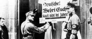 SA-Männer kleben ein Plakat mit der Aufschrift "Deutsche! Wehrt Euch! Kauft nicht bei Juden" an die Schaufensterscheibe eines Geschäfts, das in jüdischem Besitz ist. 
