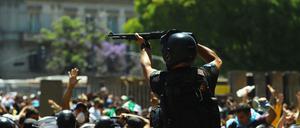 Ein Polizist hält eine Waffe hoch, als Menschen während der Totenwache für Diego Maradona mit der Polizei zusammenstoßen.