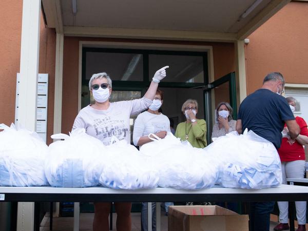 Frauen, die Schutzmasken tragen, stehen hinter einem Tisch, auf dem Säcke mit Schutzmasken liegen.