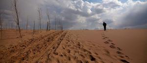 Ein Mann geht über eine weite Sandfläche