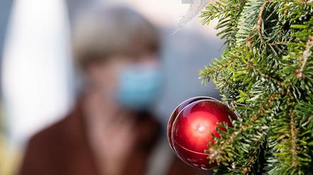 Passantin mit Mund- und Nasenmaske geht hinter einer Weihnachtsbaumkugel vorbei.