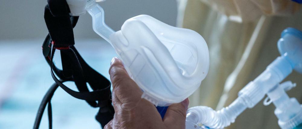 Eine Maske zur Beatmung hält im besonders geschützten Teil der Intensivstation des Universitätsklinikums Greifswald ein Covid-19-Patient in seinen Händen.
