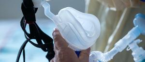 Eine Maske zur Beatmung hält im besonders geschützten Teil der Intensivstation des Universitätsklinikums Greifswald ein Covid-19-Patient in seinen Händen.