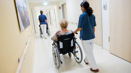 Zwei Pflegerinnen schieben Patienten mit Rollstühlen durch einen Flur. 