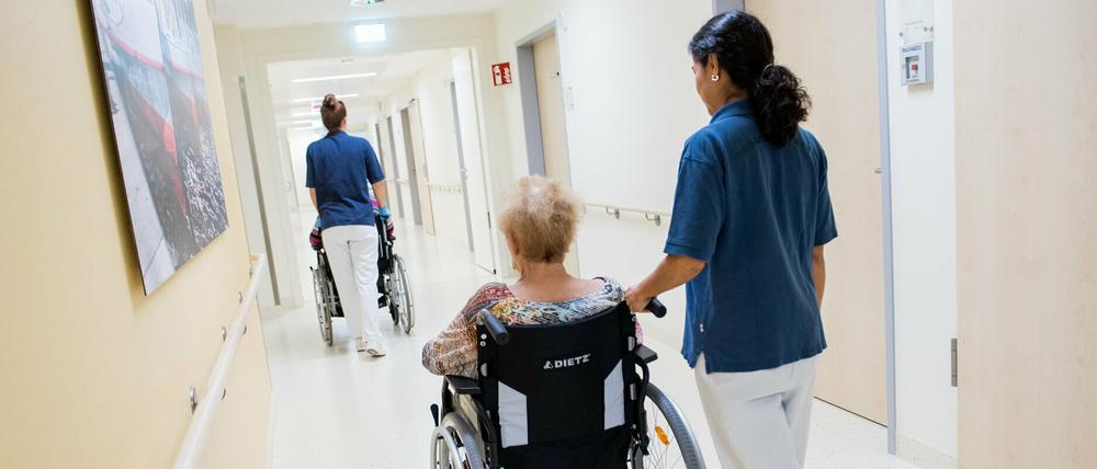 Zwei Pflegerinnen schieben Patienten mit Rollstühlen durch einen Flur.