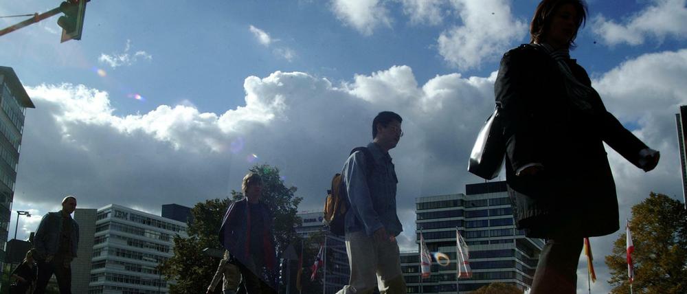 Studierende gehen im Gegenlicht auf einem Fußgängerweg vor Unigebäuden entlang.