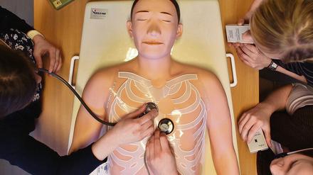 Drei Studentinnen üben mit Stethoskopen an einer Übungspuppe aus Kunststoff.