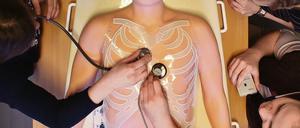 Drei Studentinnen üben mit Stethoskopen an einer Übungspuppe aus Kunststoff.