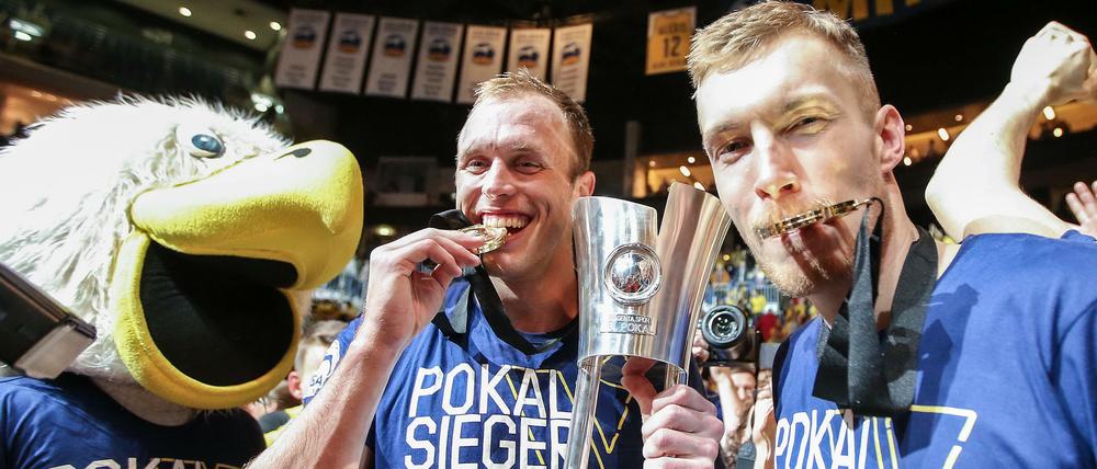 Endlich mal was Bissfestes. Luke Sikma (Mitte) feiert den Pokalsieg mit Niels Giffey (rechts) und dem Maskottchen. 