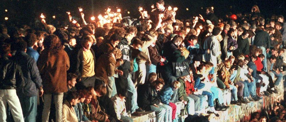 Jubelnde Menschen sitzen mit Wunderkerzen auf der Berliner Mauer am 11.11.1989.