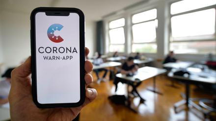 Hand hält Smartphone mit Corona-Warnapp vor Schulklasse.