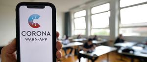 Hand hält Smartphone mit Corona-Warnapp vor Schulklasse.