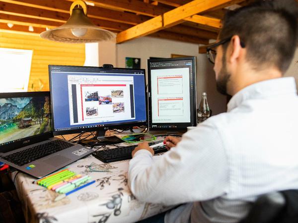 Ein Student sitzt in einer Dachwohnung vor drei Bildschirmen und verfolgt eine digitale Lehrveranstaltung.