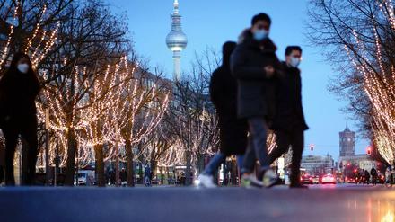 Passanten mit Mund-Nasen-Bedeckung überqueren die weihnachtlich beleuchtete Straße Unter den Linden.