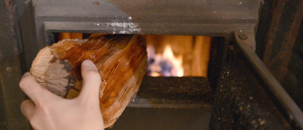 Schön gemütlich! Eine Frau tut Feuerholz in den Kachelofen.