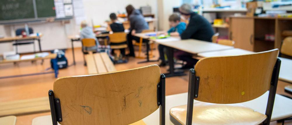 In einem fast leeren Klassenraum werden drei Kinder von zwei Lehrkräften betreut.
