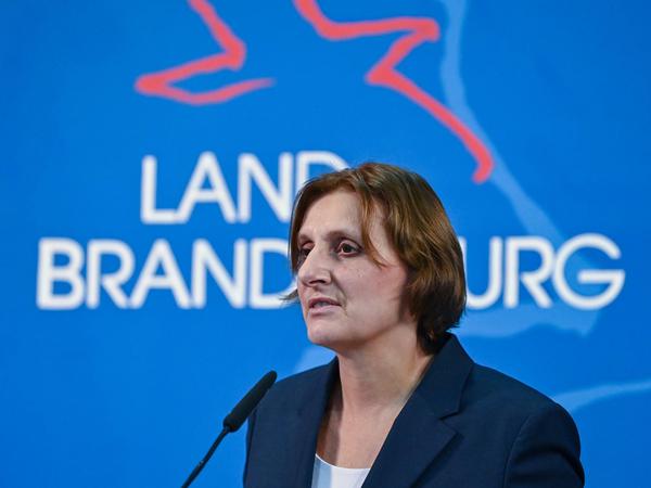 Britta Ernst spricht in ein Mikrofon, im Hintergrund ist der Schriftzug Land Brandenburg zu sehen.