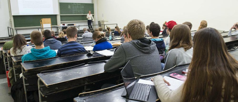 Studierende sitzen in einem Hörsaal, vorne hält eine Dozentin ihre Vorlesung.