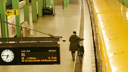 Eine Frau läuft am Alexanderplatz mit dem Fahrrad an einer U-Bahn entlang.