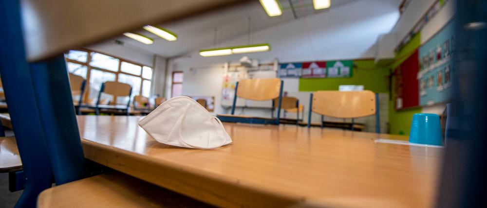 In einem leeren Klassenraum einer Grundschule sind die Stühle auf die Bänke gestellt. Eine Maske liegt auf einem Tisch.
