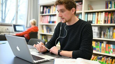 In einem Lehrerzimmer arbeitet ein Lehrer am Laptop, im Hintergrund sitzt eine Kollegin am Desktop.