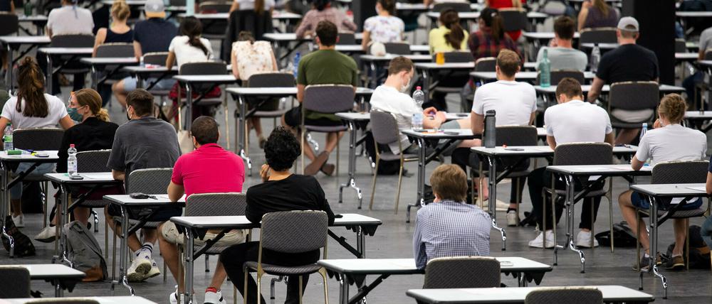 Studierende in Köln sitzen an Tischen in einer Messehalle und warten auf den Beginn ihrer Klausur.