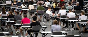 Studierende in Köln sitzen an Tischen in einer Messehalle und warten auf den Beginn ihrer Klausur.
