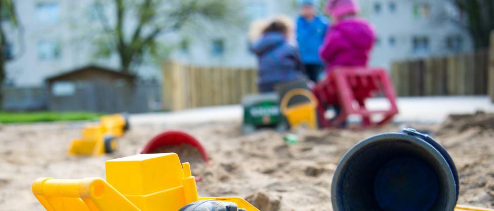 Spielzeug liegt in einem Sandkasten während Kinder in einer Kindertagesstätte spielen.