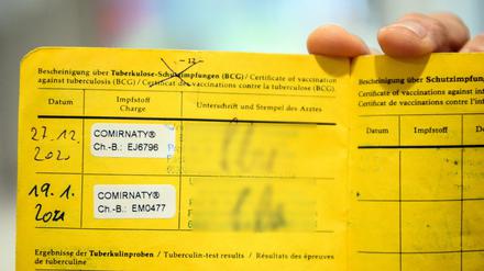 -Eine Person hält einen gelben Impfpass mit den Aufklebern vom Biontech-Pfizer-Impfstoff.