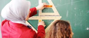 Eine Lehrerin mit Kopftuch steht mit einer Schülerin vor der Tafel.