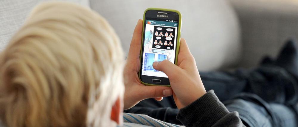 Ein Kind liegt auf einem Sofa und blickt auf sein Smartphone, stundenlang. Derzeit Alltag in vielen Familien.