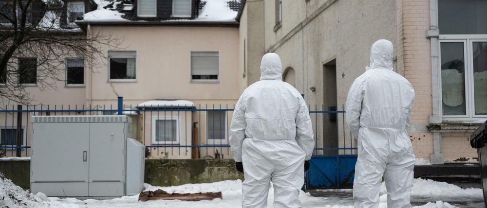 Zwei Einsatzkräfte der Polizei stehen vor einem Gebäude und tragen Schutzanzüge.