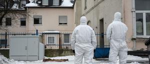 Zwei Einsatzkräfte der Polizei stehen vor einem Gebäude und tragen Schutzanzüge.