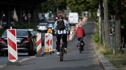 Radfahrer sind auf dem Pop-up-Radweg am Halleschen Ufer unterwegs, während ein Pkw verbotswidrig auf der Fahrbahn daneben parkt.
