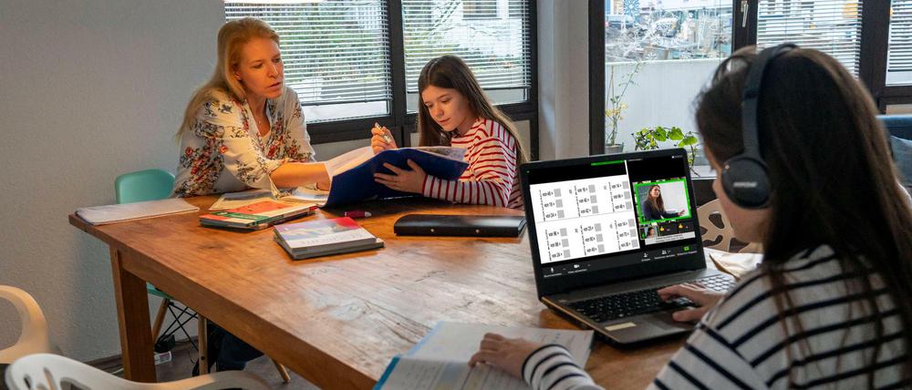 Eine Mutter betreut ihre beiden Töchter am Esstisch beim Homeschooling.