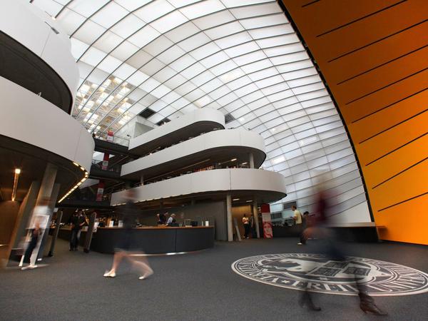 Studierende und Wissenschafter:innen laufen durch das Foyer einer Bibliothek.