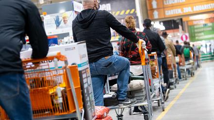 Kunden stehen mit Einkaufswagen in einem Hornbach-Baumarkt in einer Schlange vor den Kassen an.