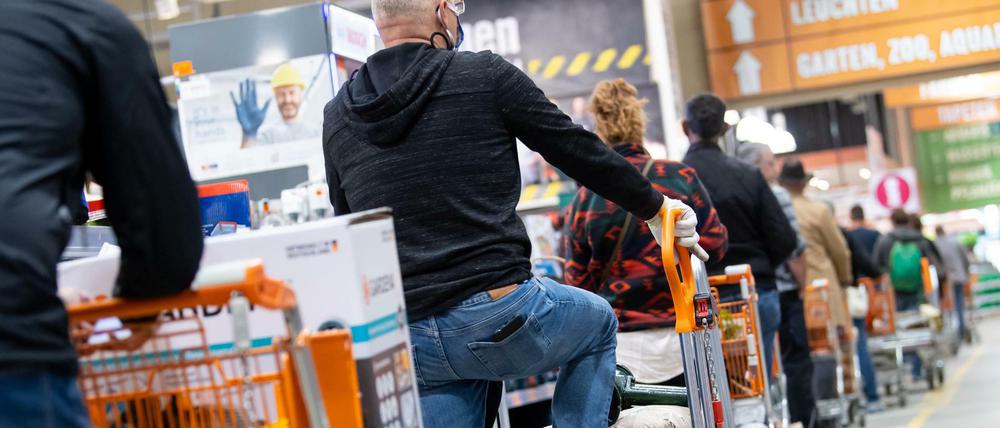 Kunden stehen mit Einkaufswagen in einem Hornbach-Baumarkt in einer Schlange vor den Kassen an.