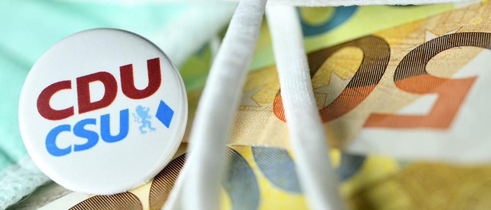 Anstecker von CDU und CSU zwischen Schutzmasken, Geldscheinen und Euromünzen.