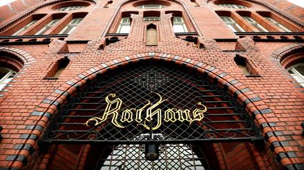 Rote Backsteinfassade des Rathauses Berlin-Lichtenberg, mit geschwungen altertümlichem "Rathaus"-Schriftzug am Tor.