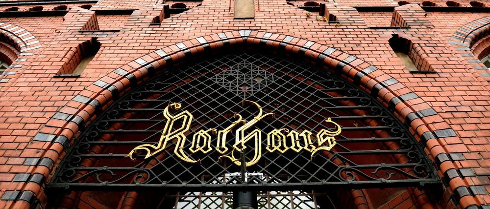 Rote Backsteinfassade des Rathauses Berlin-Lichtenberg, mit geschwungen altertümlichem "Rathaus"-Schriftzug am Tor.
