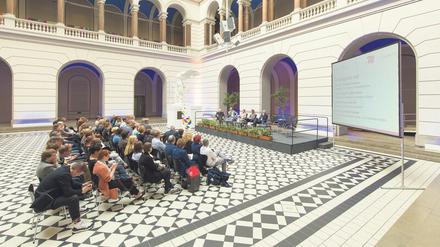 Im Lichthof der TU Berlin nehmen Wissenschaftler:innen an einer Podiumsdiskussion vor Publikum teil.